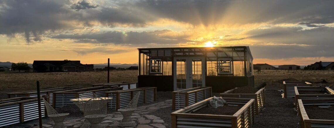 Sunset and scattered clouds behind a greenhouse within a raised bed garden with gravel and flagstone pathways
