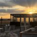 Sunset and scattered clouds behind a greenhouse within a raised bed garden with gravel and flagstone pathways